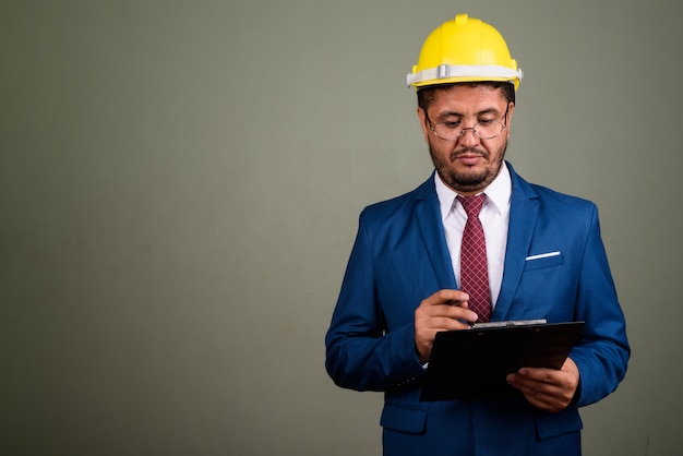 Studio shot of bearded businessman wearing suit and hardhat against colored