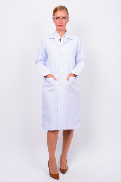 Photo studio shot of beautiful blonde woman doctor as scientist with protective glasses against white background