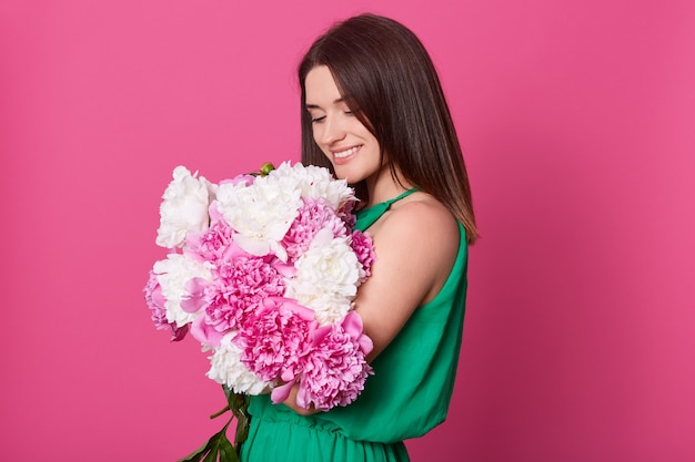 Photo studio shot of beautiful brunette girl embracing big bouquet with pink and white peonies