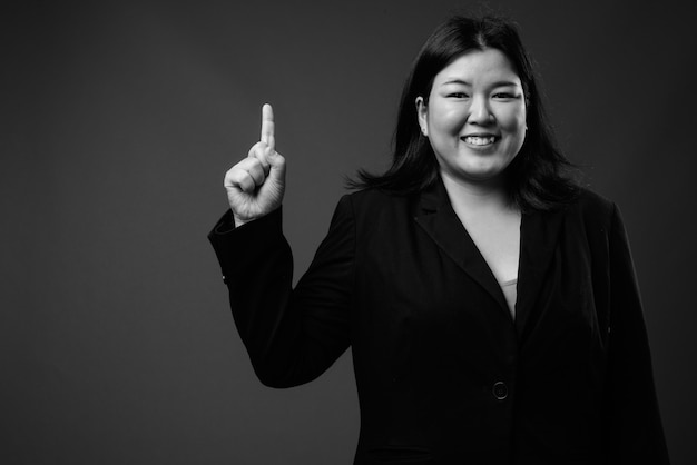 Studio shot of beautiful overweight Asian businesswoman against gray background in black and white