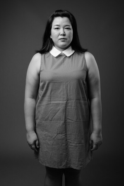 Studio shot of beautiful overweight Asian woman wearing dress against gray background in black and white