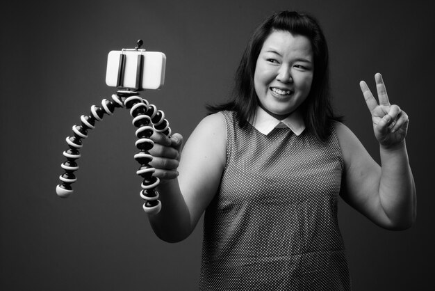 Studio shot of beautiful overweight Asian woman wearing dress against gray background in black and white