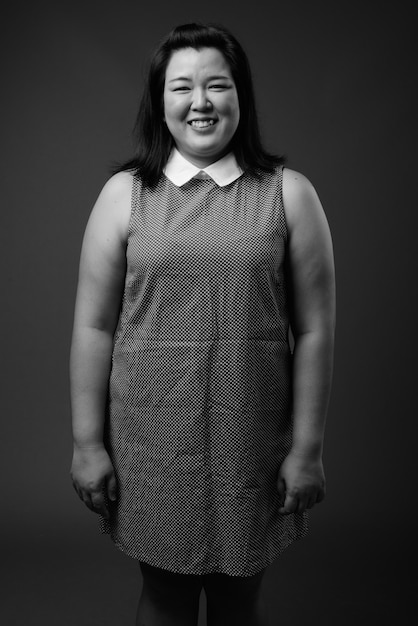 Studio shot of beautiful overweight Asian woman wearing dress against gray background in black and white