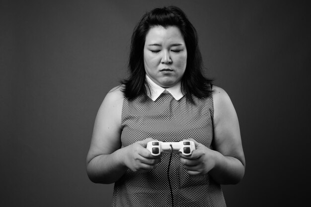 Studio shot of beautiful overweight Asian woman wearing dress against gray background in black and white