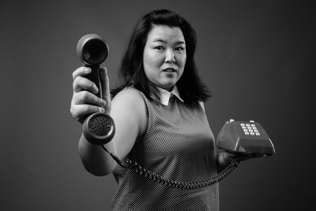 Foto studio shot di bella donna asiatica in sovrappeso che indossa un abito su sfondo grigio in bianco e nero