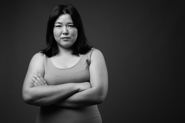 Studio shot of beautiful overweight Asian woman wearing sleeveless dress against gray background in black and white