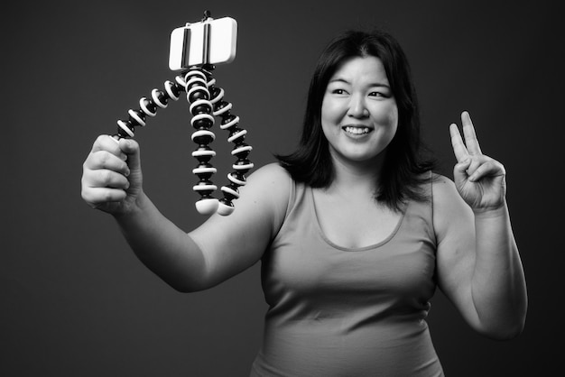 Studio shot of beautiful overweight Asian woman wearing sleeveless dress against gray background in black and white