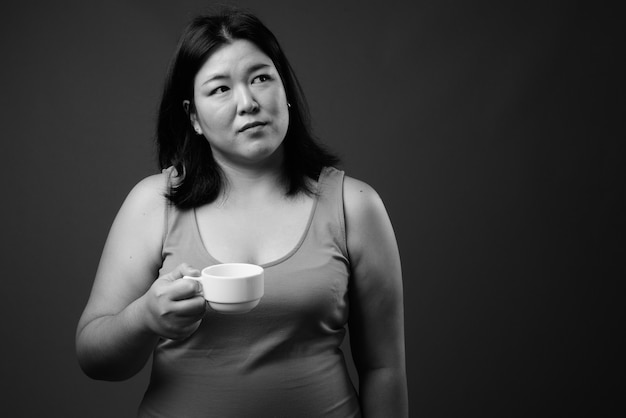 Studio shot of beautiful overweight Asian woman wearing sleeveless dress against gray background in black and white