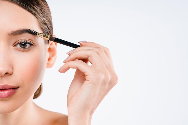 Studio shot of beautiful young woman having makeup on her eyebrow applying