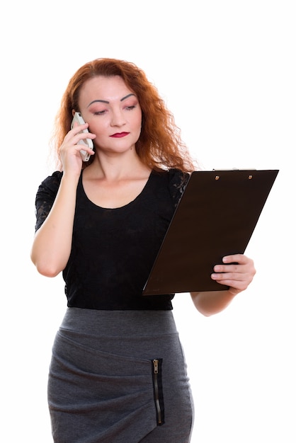 Студийный снимок бизнес-леди, читающей в буфере обмена во время разговора по мобильному телефону