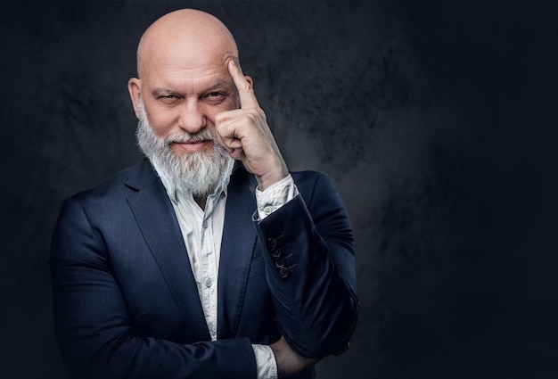 Studio shot of confident senior dressed in suit pointing his finger to his head.