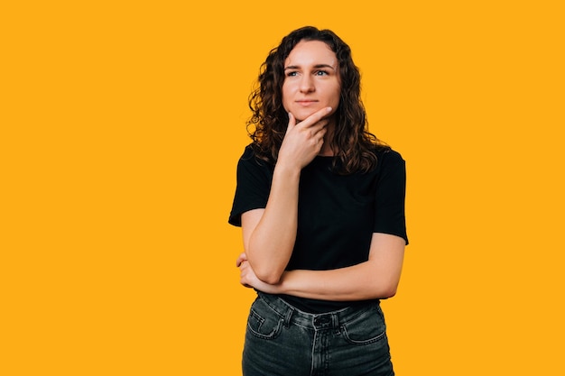 Studio shot of a curly woman standing and thinking while touching her chin