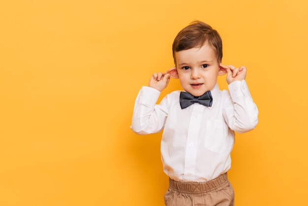 A studio shot of a cute little boy grimacing stands on a yellow background. Funny kid