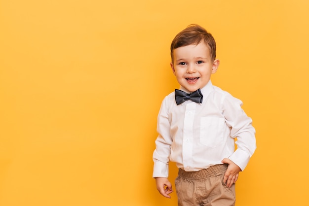 A studio shot of a cute little boy grimacing stands on a yellow background. Funny kid