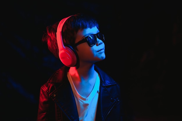 Studio shot in dark studio with neon light. Portrait of a stylish boy with headphones