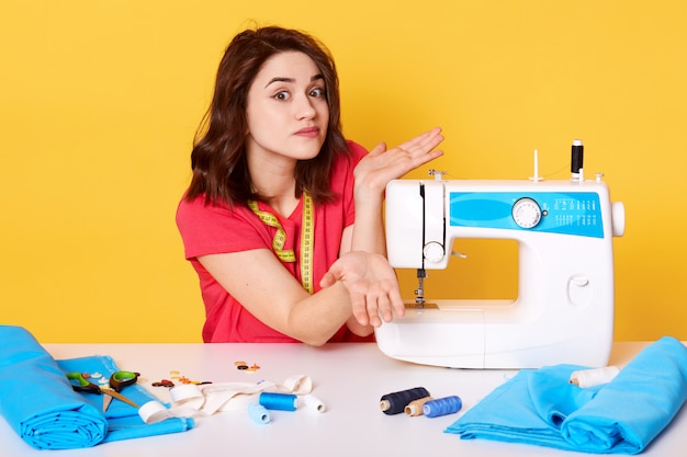 Studio shot of girl seamstress sitting at white desk with sewing machine