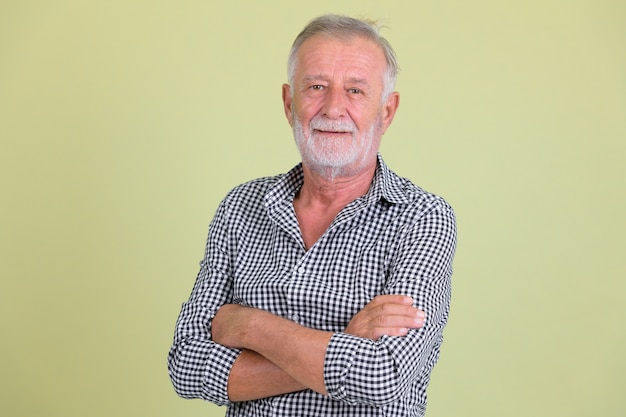 Studio shot of handsome senior bearded man against colored background