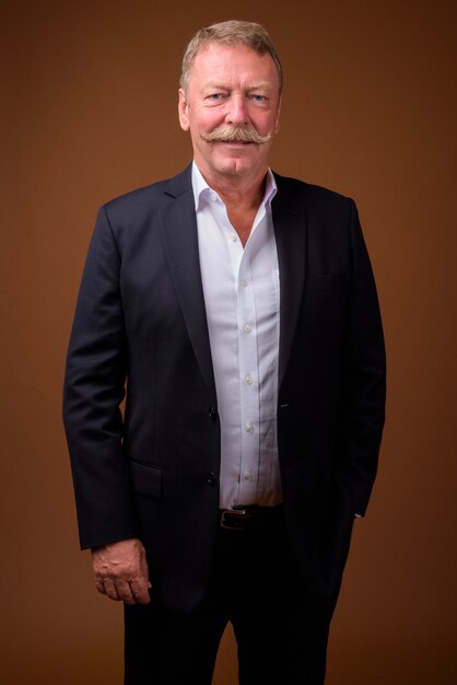 Studio shot of handsome senior businessman with mustache against brown