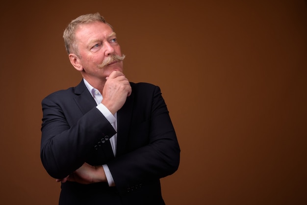 Studio shot of handsome senior businessman with mustache against brown