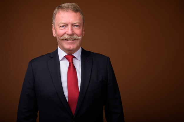 Studio shot of handsome senior businessman with mustache against brown