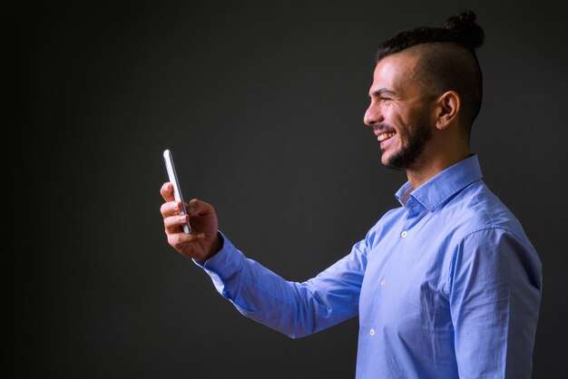 Studio shot of handsome Turkish businessman using mobile phone against gray background