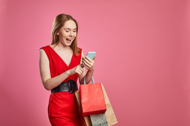 Studio shot of happy woman shopper holding shopping bags using mobile apps for online shopping