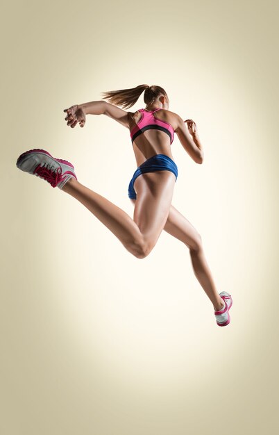 Lo studio di un atleta di salto in alto o di una donna in forma in azione isolato su sfondo grigio