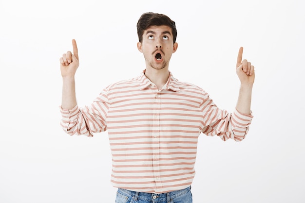 Studio shot of impressed good-looking european guy with moustache, dropping jaw and pointing upwards