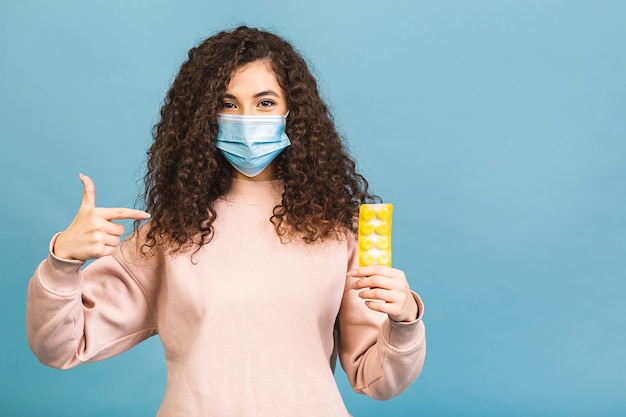 Studio shot of infected woman with pills in hands, lady wearing protective face mask