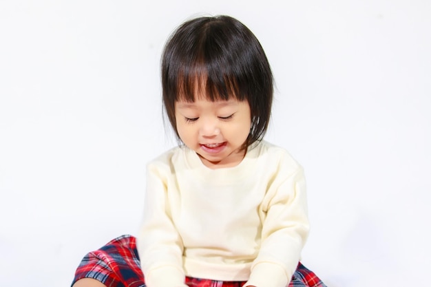 Studio shot of little cute short black hair Asian baby girl daughter model in casual plaid skirt sitting and smiling on white background