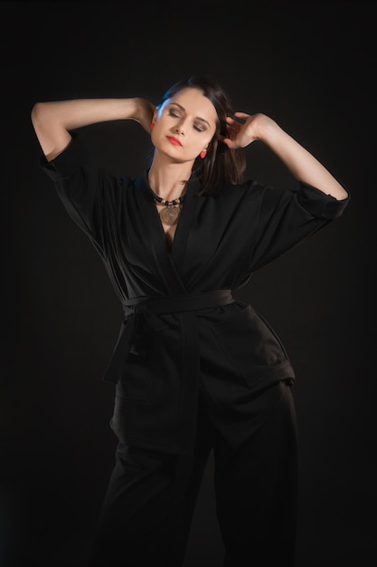 Studio shot in low key with woman with raised hands in black clothes