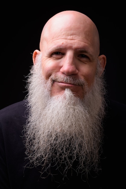 Studio shot of mature bald bearded man against black background