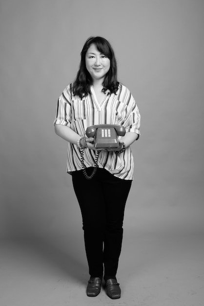 Studio shot of mature beautiful Japanese woman against gray in black and white