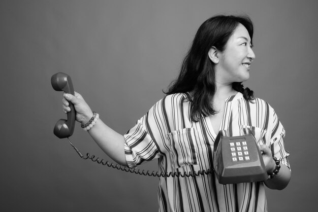 Studio shot of mature beautiful Japanese woman against gray in black and white