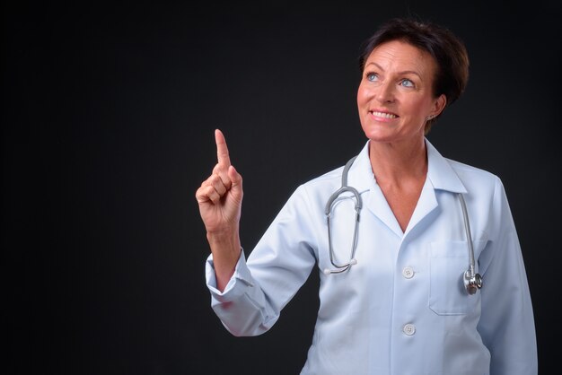 Studio shot of mature beautiful Scandinavian woman doctor with short hair against black background