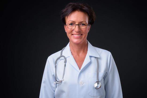 Studio shot of mature beautiful Scandinavian woman doctor with short hair against black background