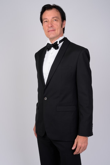 Studio shot of mature handsome businessman wearing tuxedo against white