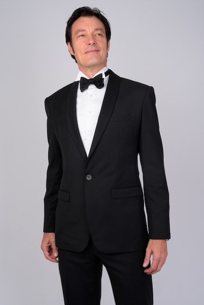 Studio shot of mature handsome businessman wearing tuxedo against white