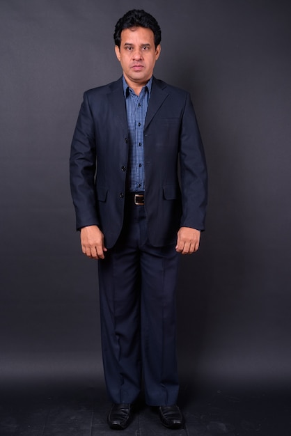 Studio shot of mature handsome Indian businessman in suit against black background