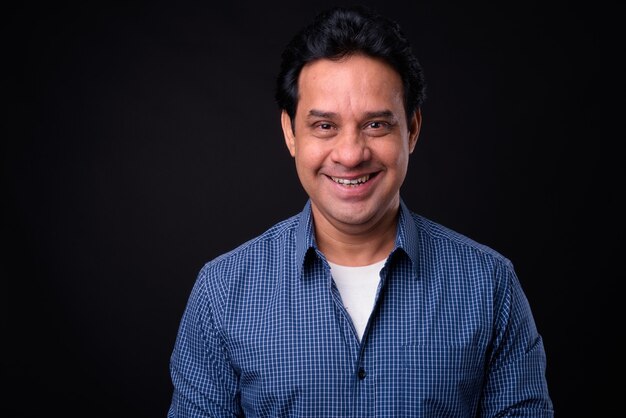 Studio shot of mature handsome Indian man against black background