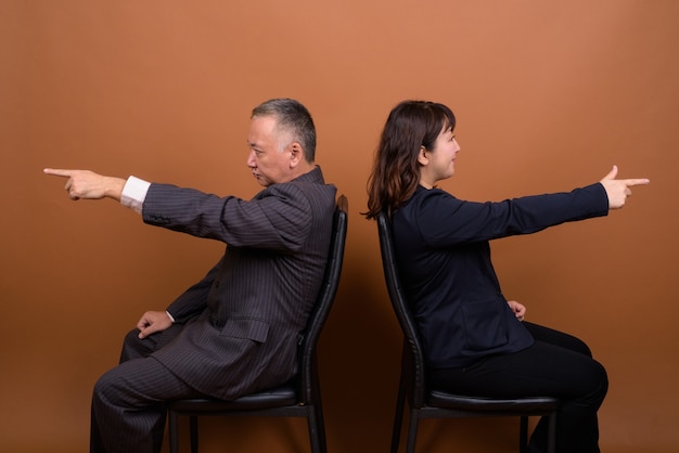 Studio shot of mature Japanese businessman and mature Japanese businesswoman together against brown background