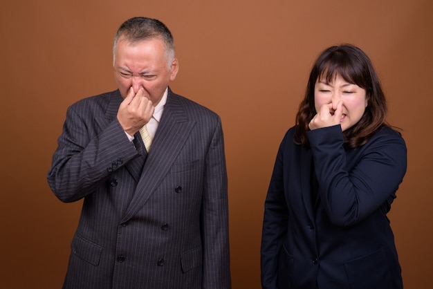 Studio shot of mature Japanese businessman and mature Japanese businesswoman together against brown background