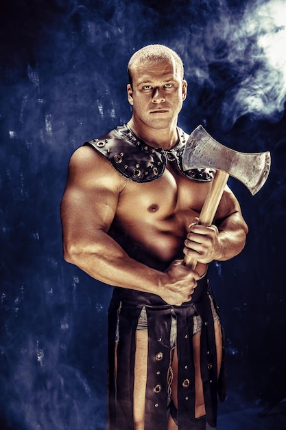 Studio shot of muscular ancient warrior man posing with axe