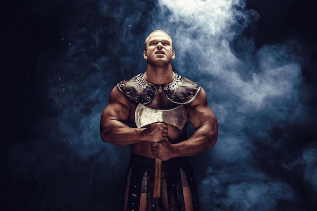 Photo studio shot of muscular ancient warrior man posing with axe