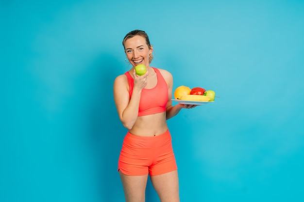 Фото Студия выстрел молодой женщины фитнеса в спортивной одежде, держа зеленое яблоко, фрукты, овощи.