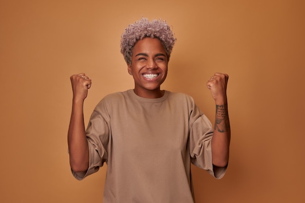 Studio shot overemotive curly african ethnic woman rejoices praises or winning competition makes fis...