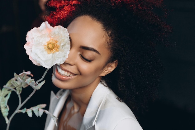 Studio shot of overjoyed dark skinned female model laughs happily and poses near flowers