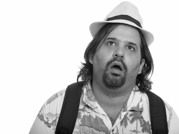 Studio shot of overweight bearded tourist man ready for vacation isolated against white background in black and white