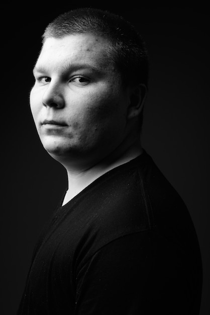 Studio shot of overweight young man against black background in black and white