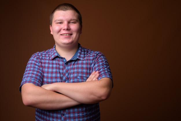 Studio shot of overweight young man wearing purple checkered shirt against brown background